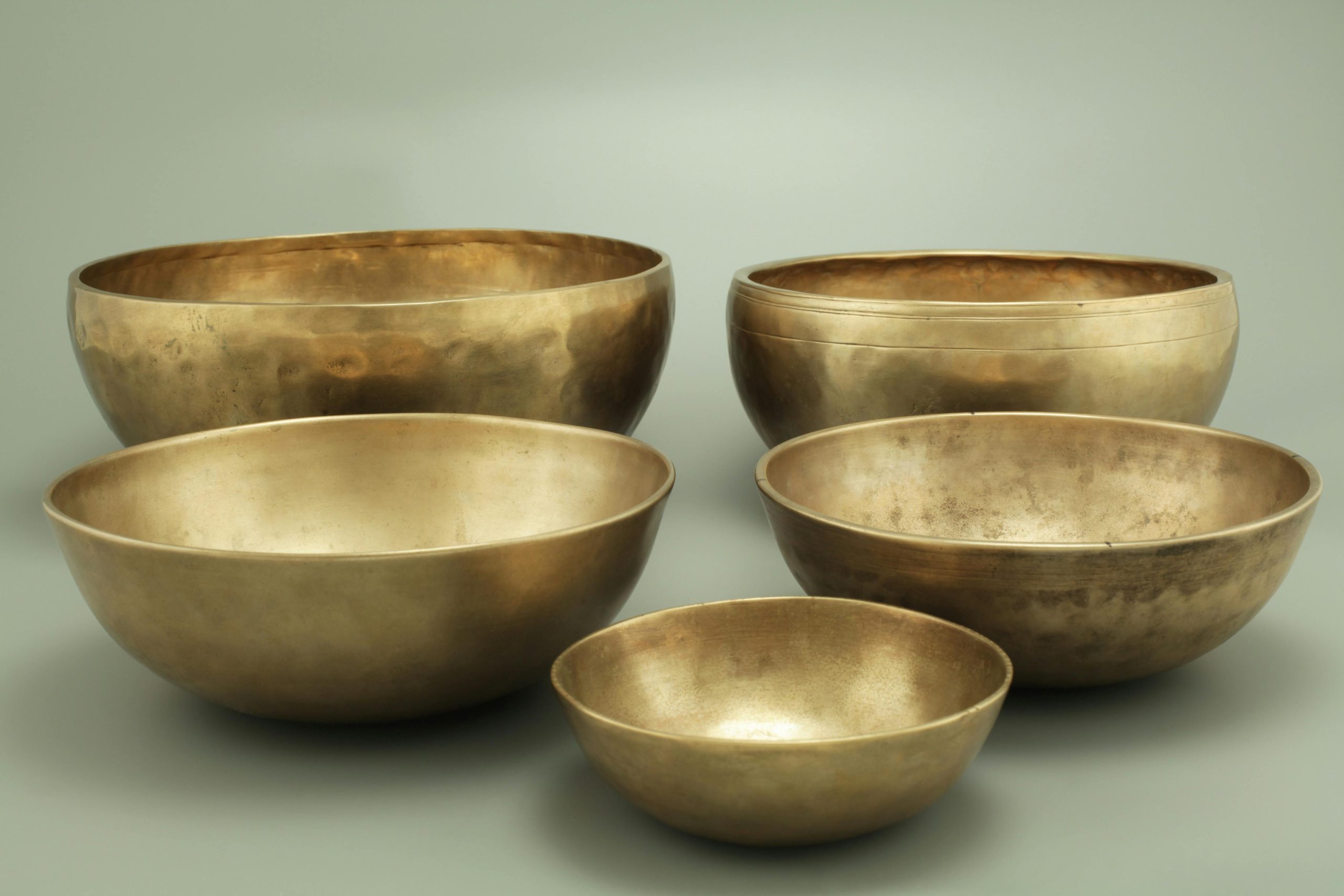 pexels-photo-3544171-3544171 Five antique brass singing bowls on a neutral gray background, creating a serene atmosphere.