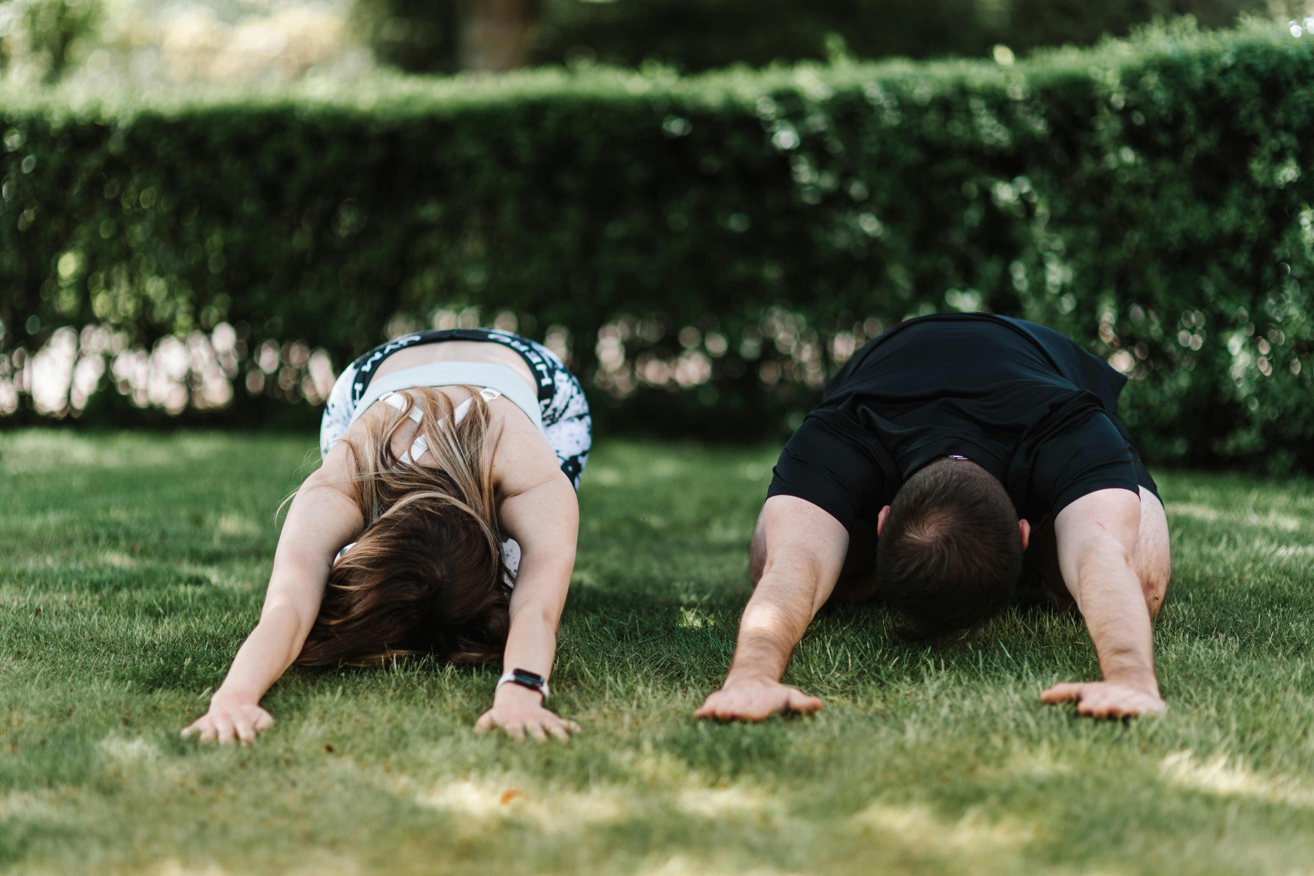 A couple practicing yoga outdoors in child's pose, enjoying nature and fitness.