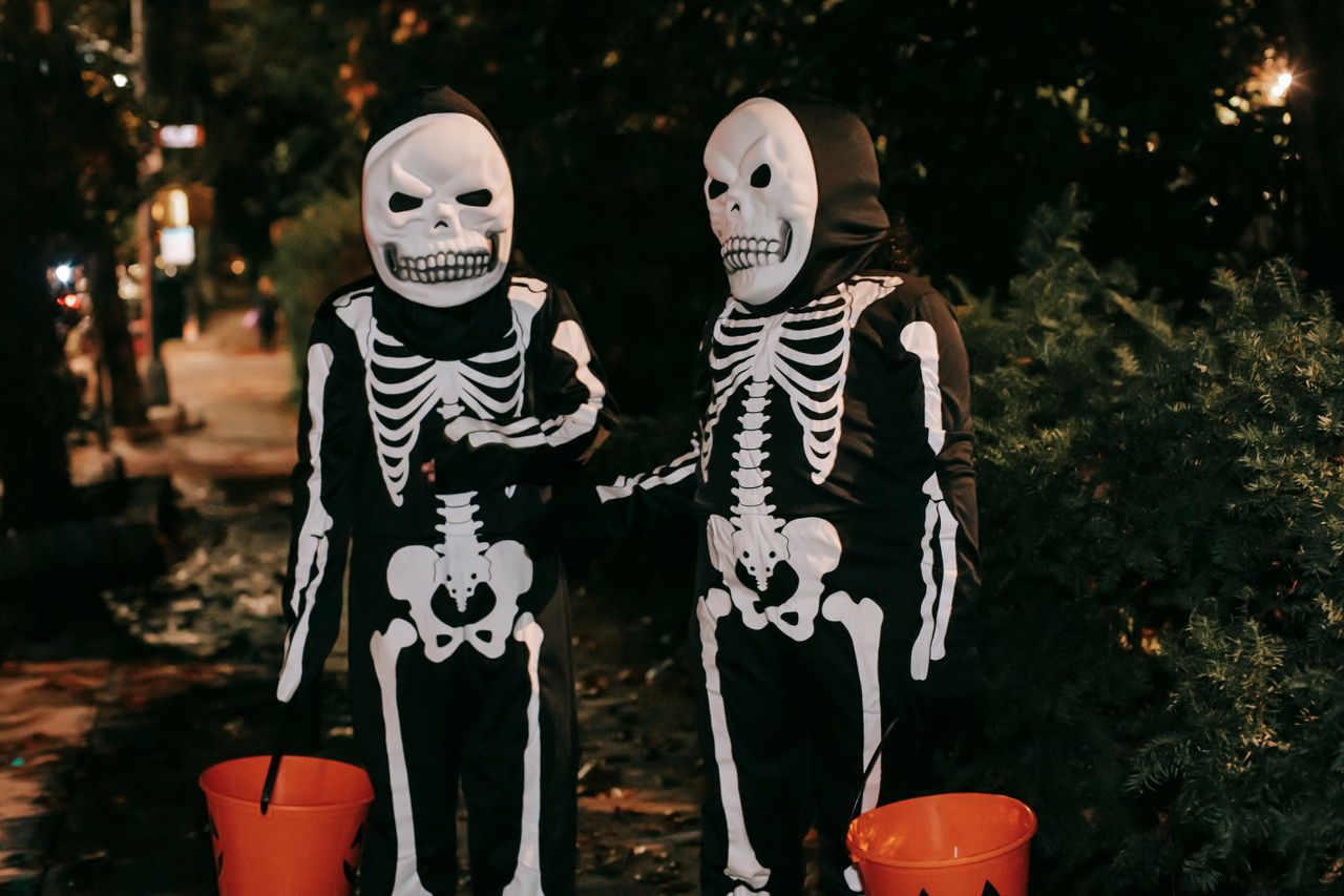 pexels-photo-5859684-5859684 Funny unrecognizable kids in skeleton costumes and masks with orange buckets in hands communicating to each other on street at Halloween night